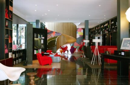 citizenM London Bankside's lobby. Gay-friendly hotel with bookshelves, red chairs, & spiral stairs. Modern design for gay men travel.
