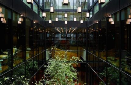 citizenM London Bankside's atrium. A gay-friendly hotel with a modern design, featuring plants, red chairs, and unique lighting fixtures.