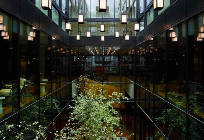 citizenM London Bankside's atrium. A gay-friendly hotel with a modern design, featuring plants, red chairs, and unique lighting fixtures.