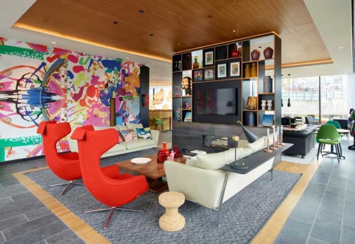 citizenM London Shoreditch gay-friendly hotel lobby. Modern design with colorful wall art, red chairs, and stylish furniture.