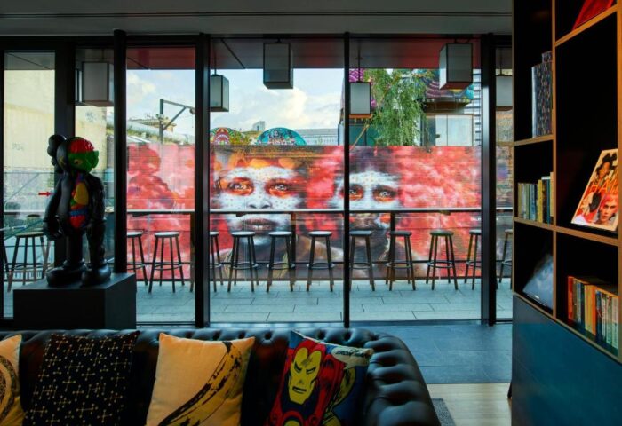 citizenM London Shoreditch gay-friendly hotel interior. Graffiti art, stools, and a black leather couch with comic book pillows. Modern design.