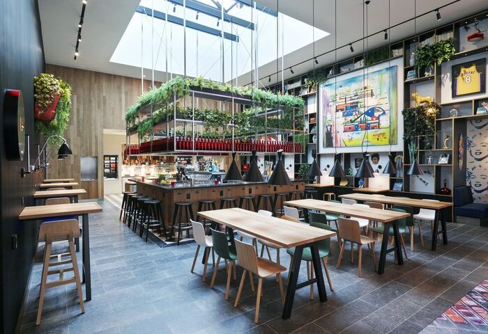 citizenM Los Angeles Downtown gay-friendly hotel bar area with tables, chairs, and greenery. Modern design with skylight. Great for gay travel.