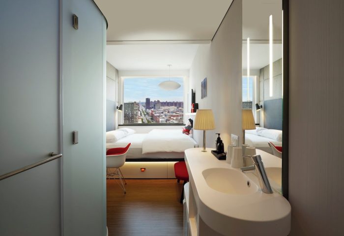 citizenM New York Bowery hotel room interior. Modern design, city view, bed, and sleek bathroom. Gay-friendly lodging for travelers.
