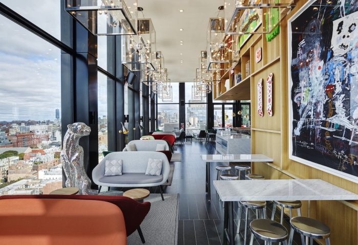 citizenM New York Bowery gay-friendly hotel interior. Lounge area with city view. Modern design, colorful sofas, and art.