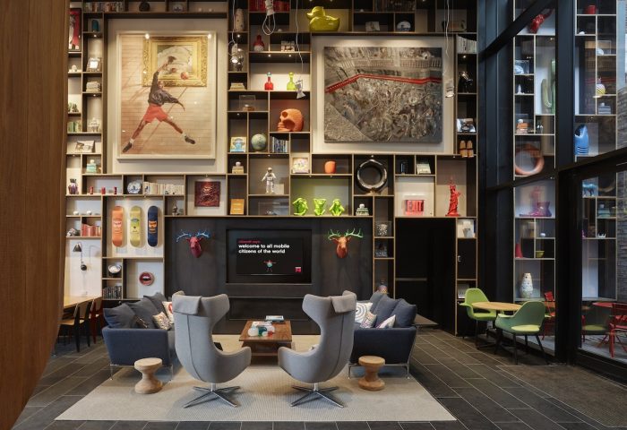 citizenM New York Bowery gay-friendly hotel lobby. Eclectic decor with art, sculptures, and books. Stylish seating area for gay travelers.