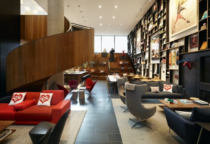 citizenM New York Bowery's stylish lobby. A gay-friendly hotel with modern design, a spiral staircase, and a wall of art. Comfy seating area.