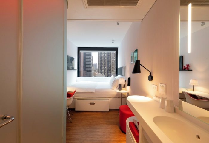 citizenM New York Times Square hotel room. Gay-friendly hotel with modern design. Room view with bed, desk, and city skyline.