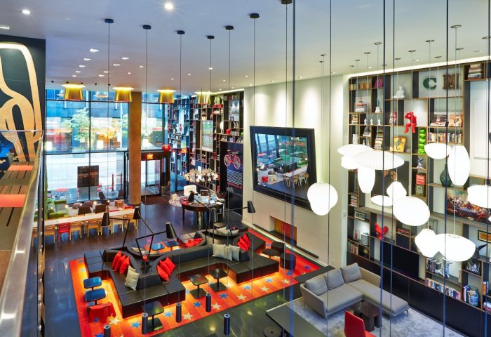citizenM New York Times Square gay-friendly hotel lobby. Stylish design, bookshelves, and comfortable seating areas. Modern, vibrant atmosphere.