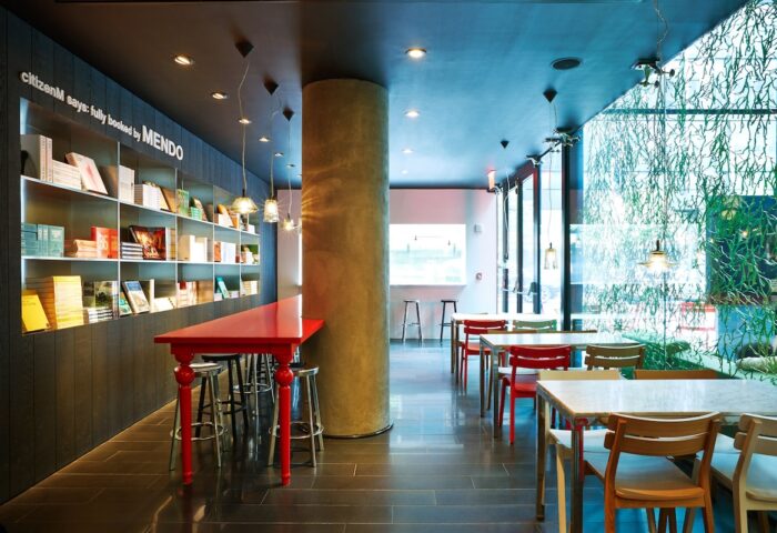 citizenM New York Times Square gay-friendly hotel interior. Tables, chairs, and a bookshelf create a stylish, welcoming space.