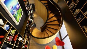 citizenM Taipei North Gate interior. Spiral staircase, colorful chairs, and shelves with art. Gay-friendly hotel design.