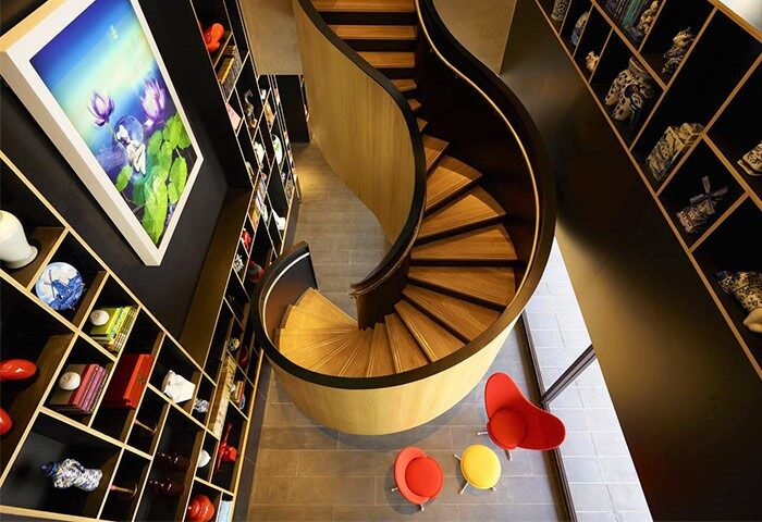 citizenM Taipei North Gate interior. Spiral staircase, colorful chairs, and shelves with art. Gay-friendly hotel design.