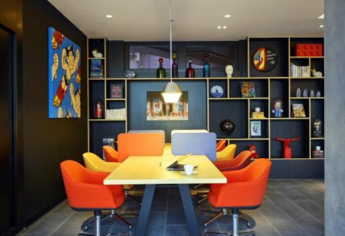 citizenM Taipei North Gate meeting room. Colorful, modern design with orange chairs, a table, and a stylish bookshelf. Gay-friendly hotel.