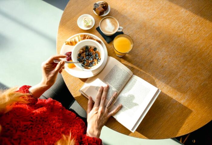 Breakfast at citizenM Tower of London. Gay-friendly hotel, woman reading a book while eating cereal, croissant, juice, and coffee.