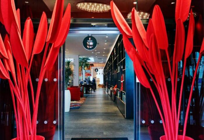 Entrance to citizenM Tower of London, a gay-friendly hotel. Red plants flank doorway. Modern interior design. Stylish, welcoming space.