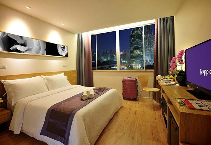 De King Boutique Hotel KLCC room. Gay-friendly hotel with a bed, desk, TV, suitcase, and a city view at night. Luxury travel.