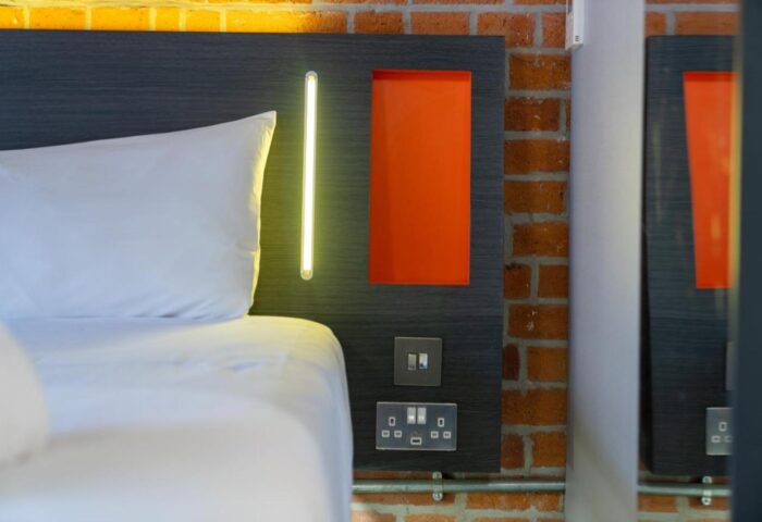 easyHotel Manchester detail. Gay-friendly hotel room with bed, headboard, orange accent, and brick wall. Modern, comfortable, and stylish.
