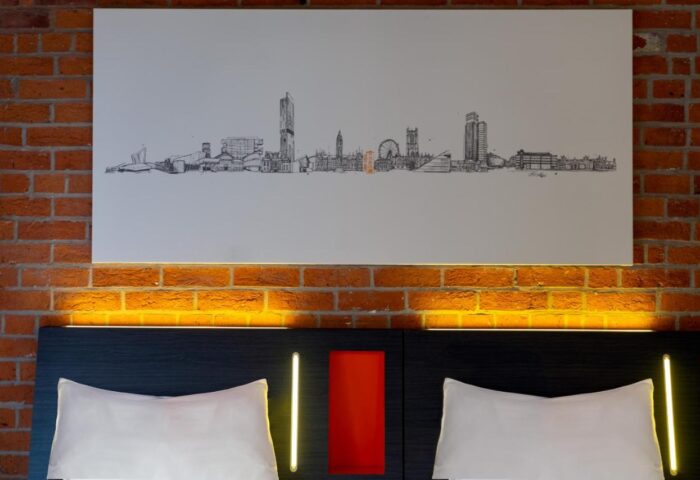 easyHotel Manchester room detail. Gay-friendly hotel with brick wall, skyline art, and pillows. A cozy stay for gay travelers in Manchester.