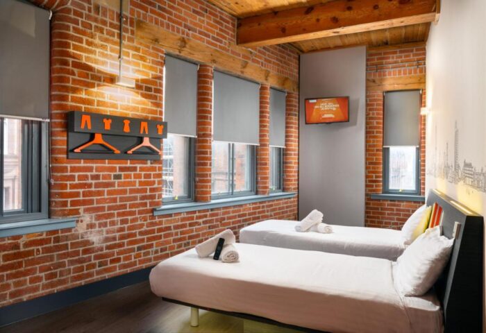 easyHotel Manchester room with twin beds, exposed brick wall, and orange accents. A gay-friendly hotel option in Manchester.