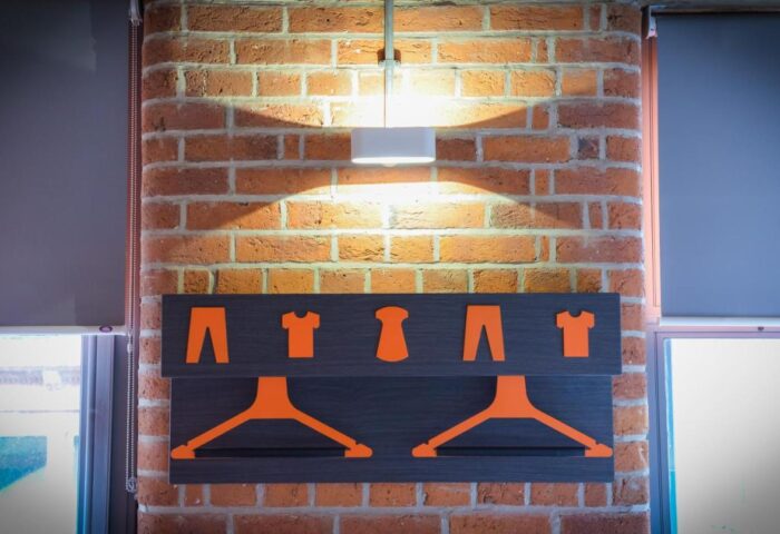 easyHotel Manchester's gay-friendly design: Clothes hanger on a brick wall. Orange icons of shirts and pants above the hangers. Modern, stylish.