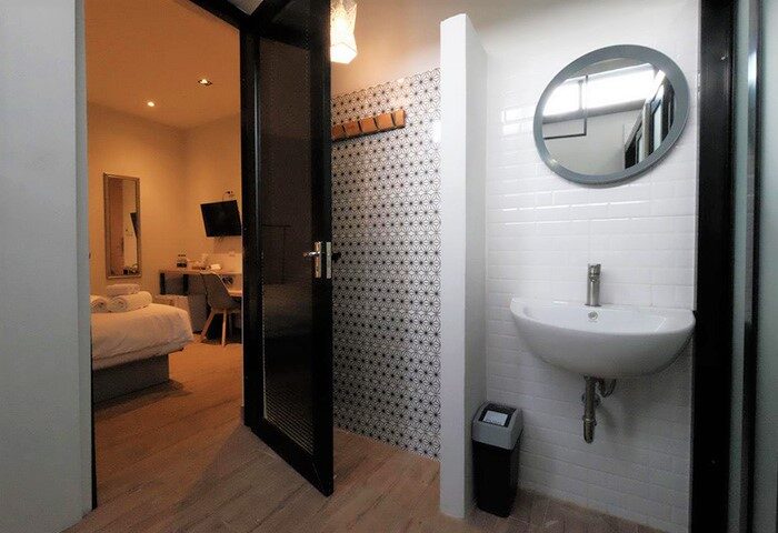 I River Chiangmai gay-friendly hotel room featuring a modern bathroom with sink, mirror, and view to the bedroom area. Thailand travel.