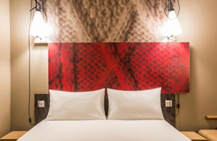 Ibis Amsterdam Centre hotel room. Pet-friendly, gay-friendly hotel with bed, pillows, red headboard, and bedside lamps. Cozy, inviting space.