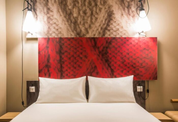 Ibis Amsterdam Centre hotel room. Pet-friendly, gay-friendly hotel with bed, pillows, red headboard, and bedside lamps. Cozy, inviting space.