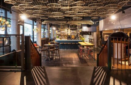 Ibis Amsterdam Centre hotel bar area with tables, chairs, and bicycle wheel ceiling decor. Gay-friendly, pet-friendly hotel interior.