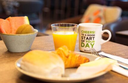 Breakfast at ibis Amsterdam Centre, a gay-friendly, pet-friendly hotel. Fruit, juice, croissant, and coffee await guests.