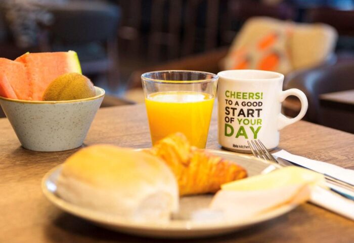 Breakfast at ibis Amsterdam Centre, a gay-friendly, pet-friendly hotel. Fruit, juice, croissant, and coffee await guests.