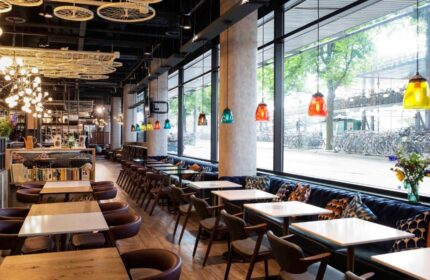 Ibis Amsterdam Centre's gay-friendly, pet-friendly hotel restaurant. Tables, chairs, and a view of bicycles outside. Interior design details.