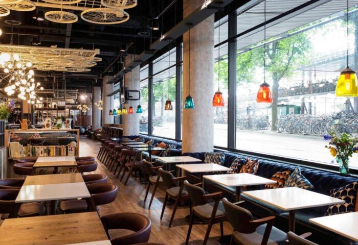 Ibis Amsterdam Centre's gay-friendly, pet-friendly hotel restaurant. Tables, chairs, and a view of bicycles outside. Interior design details.