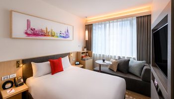 Ibis Melbourne Central gay-friendly hotel room. Queen bed, modern decor, city skyline art, and cozy seating area. Ideal for gay travelers.