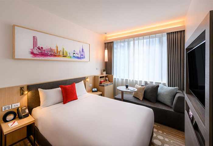 Ibis Melbourne Central gay-friendly hotel room. Queen bed, modern decor, city skyline art, and cozy seating area. Ideal for gay travelers.
