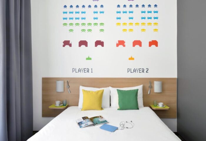 Ibis Styles Budapest Center gay-friendly hotel room. Bed with colorful pillows, retro video game wall art, and modern decor. Comfy stay in Budapest.