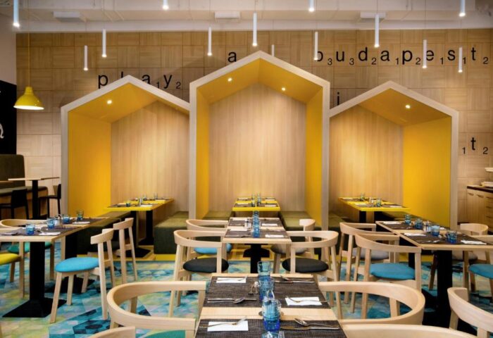 ibis Styles Budapest Center's gay-friendly hotel restaurant. Stylish dining area with tables set for meals, and cozy, yellow-accented booths.