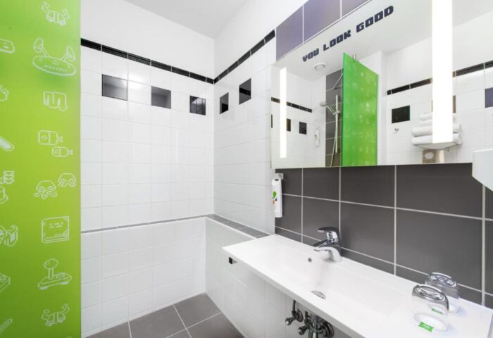 ibis Styles BUDAPEST CENTER gay-friendly hotel bathroom. White sink, gray tiles, and a mirror with You Look Good text. Green wall with pixel art.