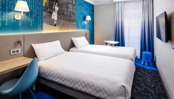 ibis Styles Manchester Portland hotel room. Two twin beds with blue themed decor. Gay-friendly hotel for gay men travel advice.