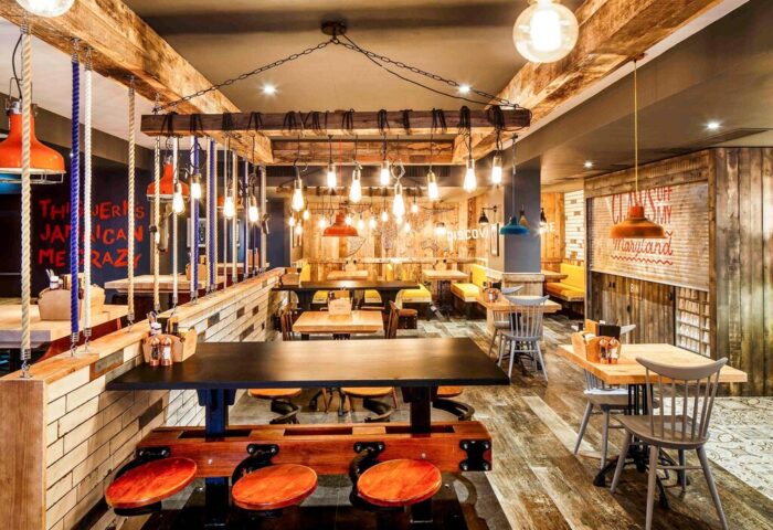 Ibis Styles Manchester Portland hotel interior. Gay-friendly hotel with rustic design, wooden beams, and hanging lights. Restaurant seating area.