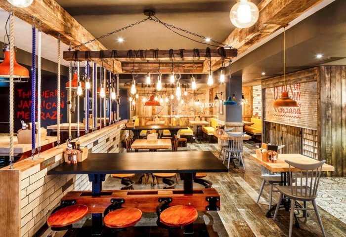 Ibis Styles Manchester Portland hotel interior. Gay-friendly hotel with rustic design, wooden beams, and hanging lights. Restaurant seating area.