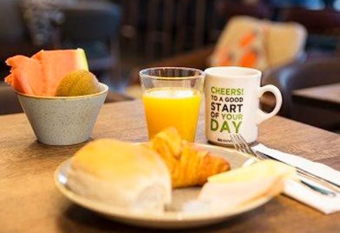 Breakfast at gay-friendly ibis Styles Manchester Portland Hotel. Fruit, juice, coffee, and pastries on a wooden table.