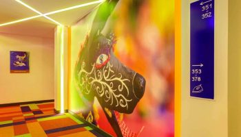 ibis Styles Mexico Reforma hallway. Colorful carpet, wall art, & room numbers. Gay-friendly hotel with modern design elements.