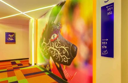 ibis Styles Mexico Reforma hallway. Colorful carpet, wall art, & room numbers. Gay-friendly hotel with modern design elements.