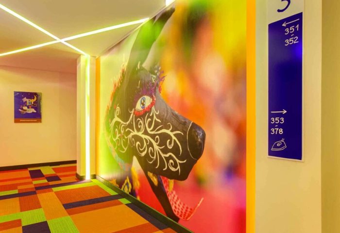 ibis Styles Mexico Reforma hallway. Colorful carpet, wall art, & room numbers. Gay-friendly hotel with modern design elements.