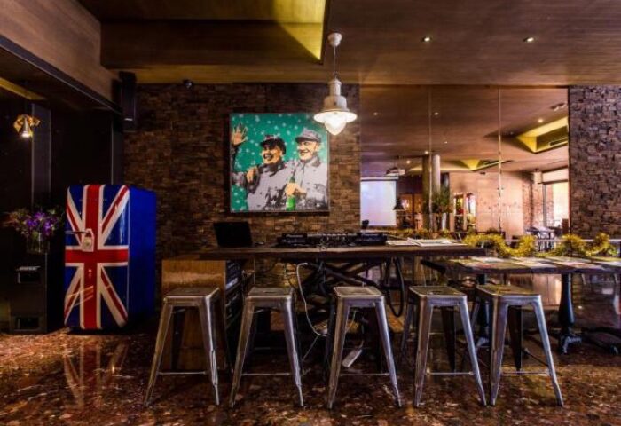 Inhouse Boutique, a gay-friendly hotel. Interior view of the bar area with stools, a table, and a refrigerator painted with the British flag.