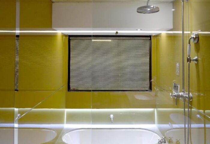 Bathroom in gay-friendly Inhouse Boutique Hotel. Features a modern shower, bathtub, and window with blinds. The room is illuminated with yellow lighting.