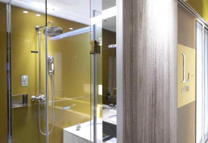Inhouse Boutique gay-friendly hotel's bathroom. Glass shower with gold accents, modern fixtures, and 'Love' detail on the door. Stylish design.