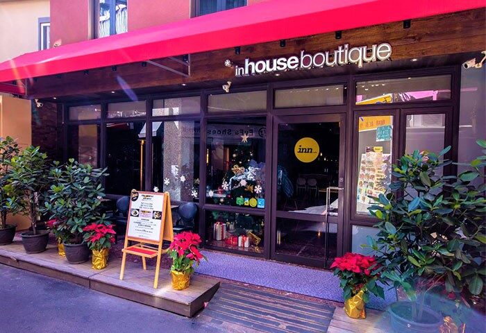 Inhouse Boutique, a gay-friendly hotel. Storefront view with red awning, plants, and Christmas decorations. Welcoming space for gay travelers.