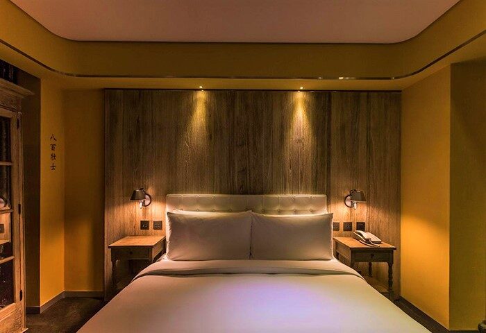 Inhouse Hotel bedroom. Gay-friendly hotel room with a bed, wooden headboard, bedside tables, and warm lighting. Modern design.