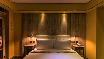Inhouse Hotel bedroom. Gay-friendly hotel room with a bed, wooden headboard, bedside tables, and warm lighting. Modern design.