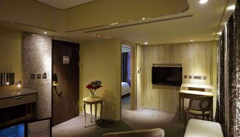 Inhouse Hotel room interior. Gay-friendly hotel features include a desk, TV, mini-fridge, and view into the bedroom. Modern design.